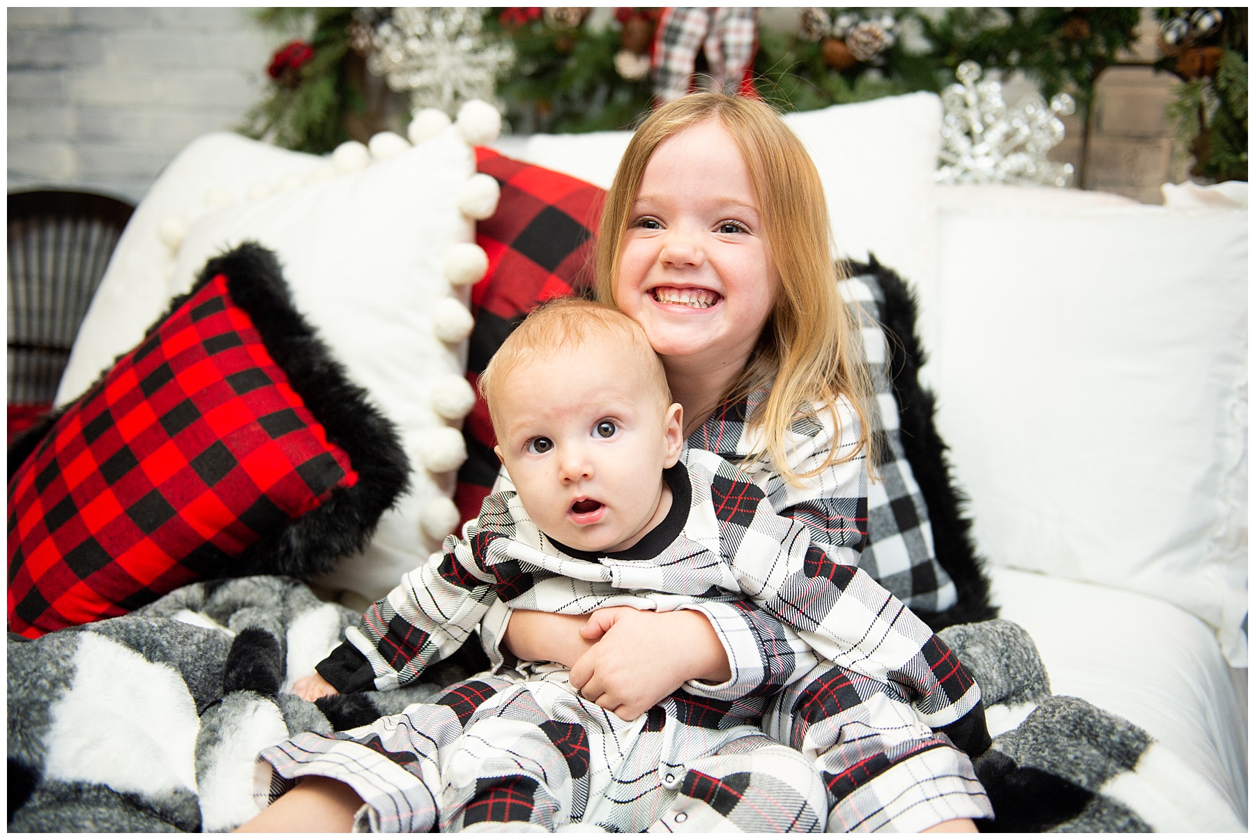 Young girl holding baby sibling in lap and smiling during indoor christmas family session with grandfather Chris Stephens