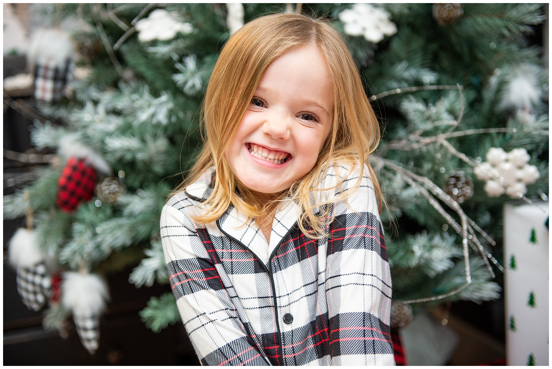 young girl smiling and posing in front of Christmas tree during indoor Christmas session