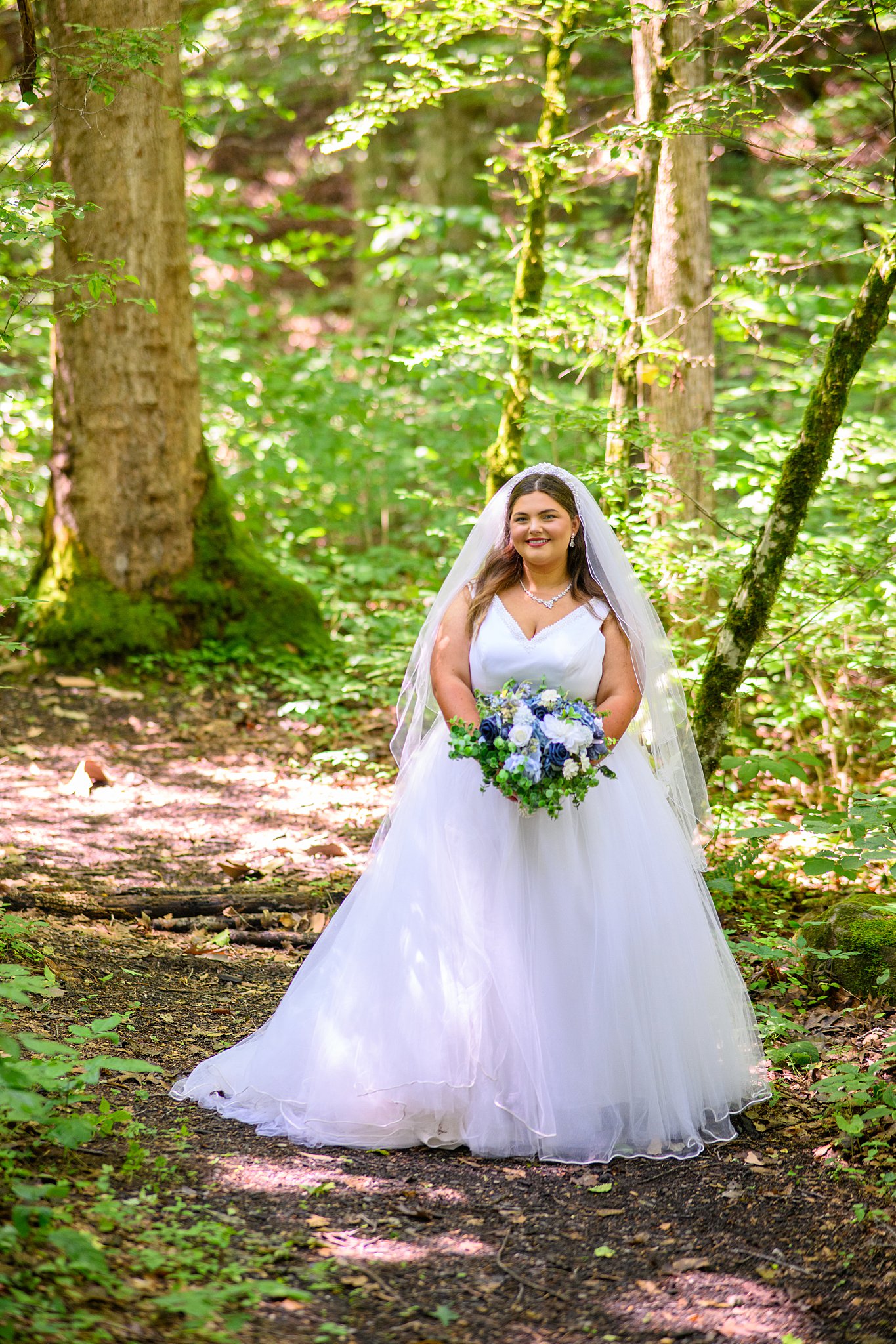 bride standing in the woods holding blue bouquet 